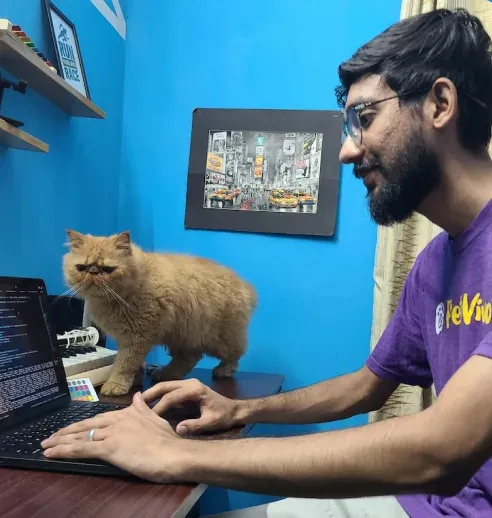 A team member working at his laptop while his orange cat sits on the desk beside him